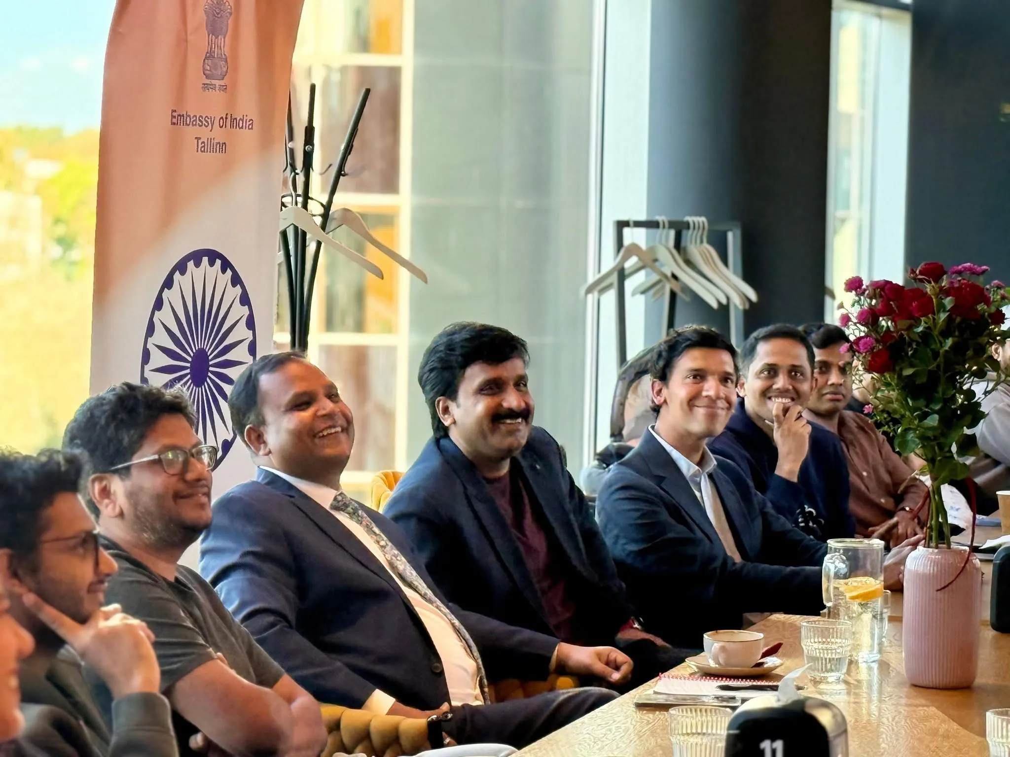 The Ambassador and guests smiling at a long table in Tartu, with an Embassy of India banner behind